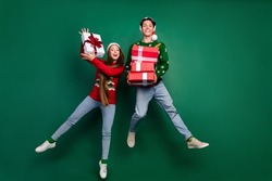 Photo of funny crazy couple hold pile giftbox enjoy jump flight wear hat ugly pullover isolated green color background