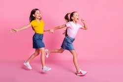 Full length body size view of two pretty cheerful girls holding hands jumping running isolated over pink pastel color background