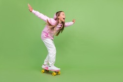 Full length photo of impressed little blond girl ride skate wear hoodie trousers sneakers isolated on green background