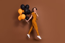 Full size photo of amazed excited young woman jump hold hands balloons go isolated on brown color background