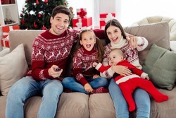 Photo of impressed cute couple two kids dressed new year pullovers sitting couch watching tv pointing finger you indoors house home room