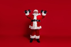 Photo of sporty active energetic old man do weight lift exercise wear santa hat costume isolated red color background