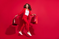 Full length profile photo of lovely brunette lady jump shopping wear suit shoes isolated on red color background