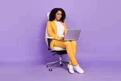 Photo of  cute woman dressed yellow suit spectacles sitting chair typing modern device isolated violet color background