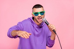 Photo of cool young brunet guy sing in mic wear eyewear hoodie isolated on pink background