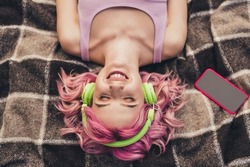 Top above high angle photo of young cheerful girl happy positive smile lying blanket listen music headphones outdoors