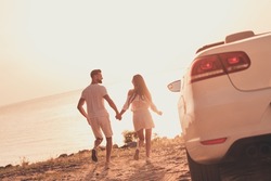 Photo of cheerful carefree married couple dressed white clothes driving car walking beach holding arms outdoors country side road