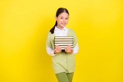 Portrait of attractive smart clever cheerful preteen girl carrying book isolated over bright yellow color background