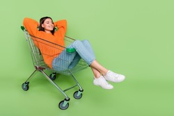 Portrait of attractive dreamy cheerful girl riding cart lying resting silence isolated over bright green color background