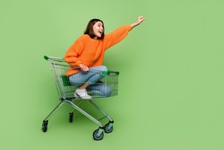 Portrait of attractive cheerful girl riding cart basket striving travel super hero isolated over bright green color background