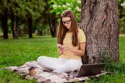 Full length body size photo woman sitting in park using smartphone wearing glasses on plaid blanket