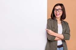 Photo of funny lady indicate finger poster empty space wear glasses khaki shirt isolated beige color background