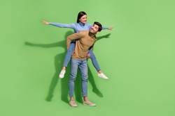 Photo of two carefree people guy carry piggyback lady show plane pose wear casual outfit isolated green color background