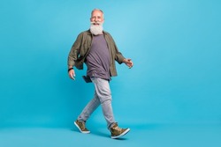 Full length profile photo of impressed old man go wearing khaki shirt jeans shoes isolated over blue color background
