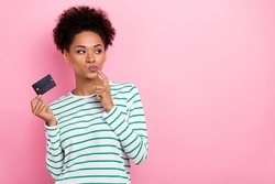 Portrait of attractive minded sly girl holding bank card thinking deciding copy space ad isolated over pink pastel color background