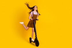 Full length body size view of attractive cheerful dreamy girl riding scooter air blowing isolated over bright yellow color background