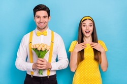 Photo of shocked lady positive man hold yellow fresh tulips look camera isolated on blue color background