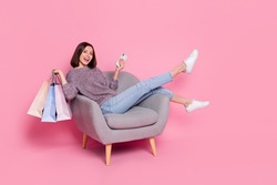 Portrait of attractive cheerful girl in armchair using device holding bags order delivery isolated over pink pastel color background