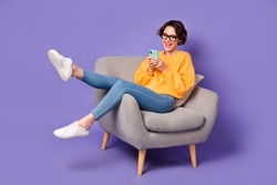Portrait of attractive cheerful girl sitting using device communicating having fun rest isolated over violet lilac color background
