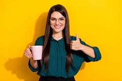 Photo of smart shiny lady dressed green shirt glasses showing thumb up drinking tea isolated yellow color background