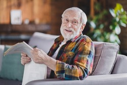 Photo of retired old man grandpa grey hair hold newspaper have break smile wear casual checkered clothes specs sit sofa indoors home room