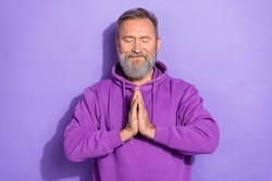 Photo of old handsome positive optimistic man dressed purple hoodie arms together praying eyes closed isolated on violet color background