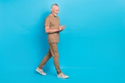 Full body profile portrait of aged person walking use telephone isolated on blue color background