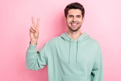 Photo of young positive toothy beaming smiling guy wear khaki hoodie showing v-sign hello friendly greetings cadre isolated on pink color background