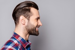 A side view portrait of young handsome smiling man with stylish haircut standing against gray background.
