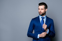 Portrait of serious fashionable handsome man in blue suit and tie  buttoning cufflinks