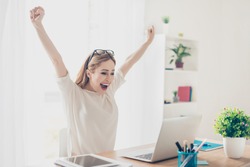 Yes! Happy excited woman at home workstation triumphing with raised hands