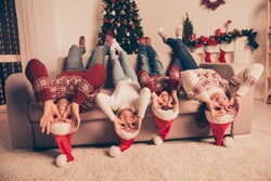 Humor, comic, funky funny friendship mode. Four cheerful relatives, married couple, siblings fooling around in knitted traditional costumes, x mas eve celebration, on couch upside down