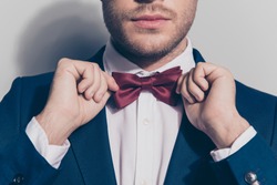Close up portrait - bearded man ties a bowtie at the collar, correcting red bow on his white shirt over grey background