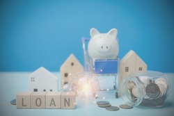 Text LOAN on wood blocks with coins. Behind have a light bulb, a little wooden house, a white piggy bank on a blue shopping cart,  all on a blue desk. Financial, Investment estate, Loan, bank Concept.