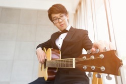 Asian student in tuxedo or elegant young fashion teenage or Young musician tuning a guitar on classroom or studio. He prepared learn Music Courses or the music competition. or audio recordings