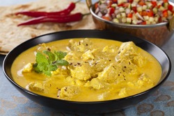 Bowl of pork curry in a creamy sauce flavoured with garlic, cinnamon, coriander, cumin, turmeric and chilli, served with kachumber Indian salad and naan bread. Could be chicken.