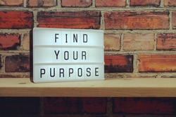 Find Your Purpose word in light box on brick wall and wooden shelves background