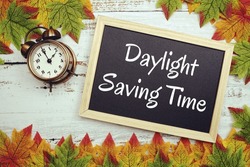 Daylight Saving Time typography text on wooden blackboard with alarm clock and maple leaves