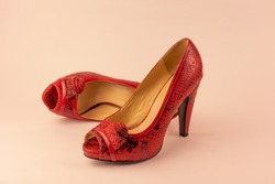 red open-toe high-heeled shoes with decorative rose on white background. One of them is lying 