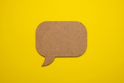 Brown wood speech bubble on yellow paper. Close up of paper blank speech bubble, isolated on yellow background with copy space for advertisement. Advertising area, mockup.