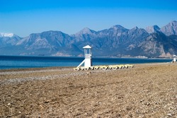 Sun loungers, lifeguard chair, snowy mountains and blue sea at Konyaaltı beach, a holiday destination in Turkey.
