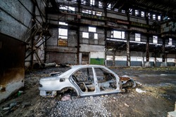 Side view of an old rusty antique car frame on the background of broken-down plant. Interior of the large abandoned building with a damaged car