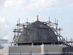   A new mosque under construction against the sunny blue sky, building a new mosque with its big dome in cement and surrounded with wood scaffold, Mosque under construction         