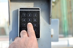 a person hand pressing a password on a numerical keypad to lock or unlock an alarm system, opening garage gate for car entry, alarm system technical electronic panel security concept, selective focus
