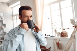 Young bearded man smiling and drinking coffee at home
