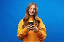 Portrait of young beautiful woman texting on the phone against blue background