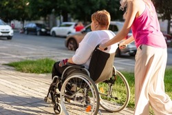 Young female caregiver pushing wheelchair with female person with disability across city street