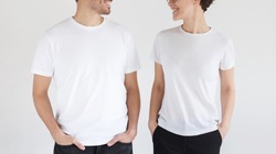 Young smiling couple in blank white t-shirts looking at each other, isolated on gray background