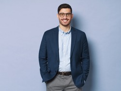 Young business man wearing formal clothes and eyeglasses, standing isolated against blue background in relaxed pose, smiling friendly