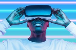 Future of education in metaverse. Young African man wearing virtual reality goggles, looking up watching interactive video tutorial with visual effects of augmented reality